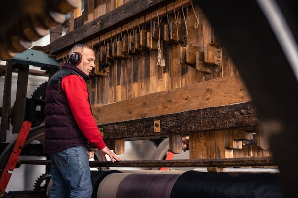 a man creating beetled linen on a large wooden press
